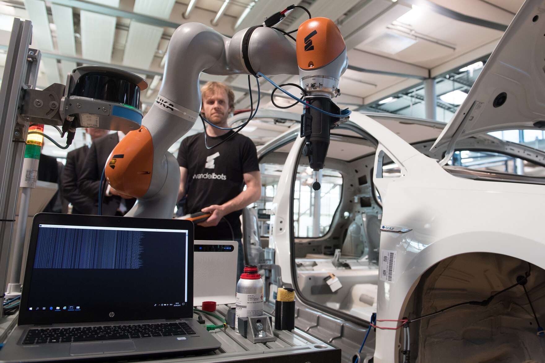 Ein Roboter und ein Mann arbeiten an einem Auto.