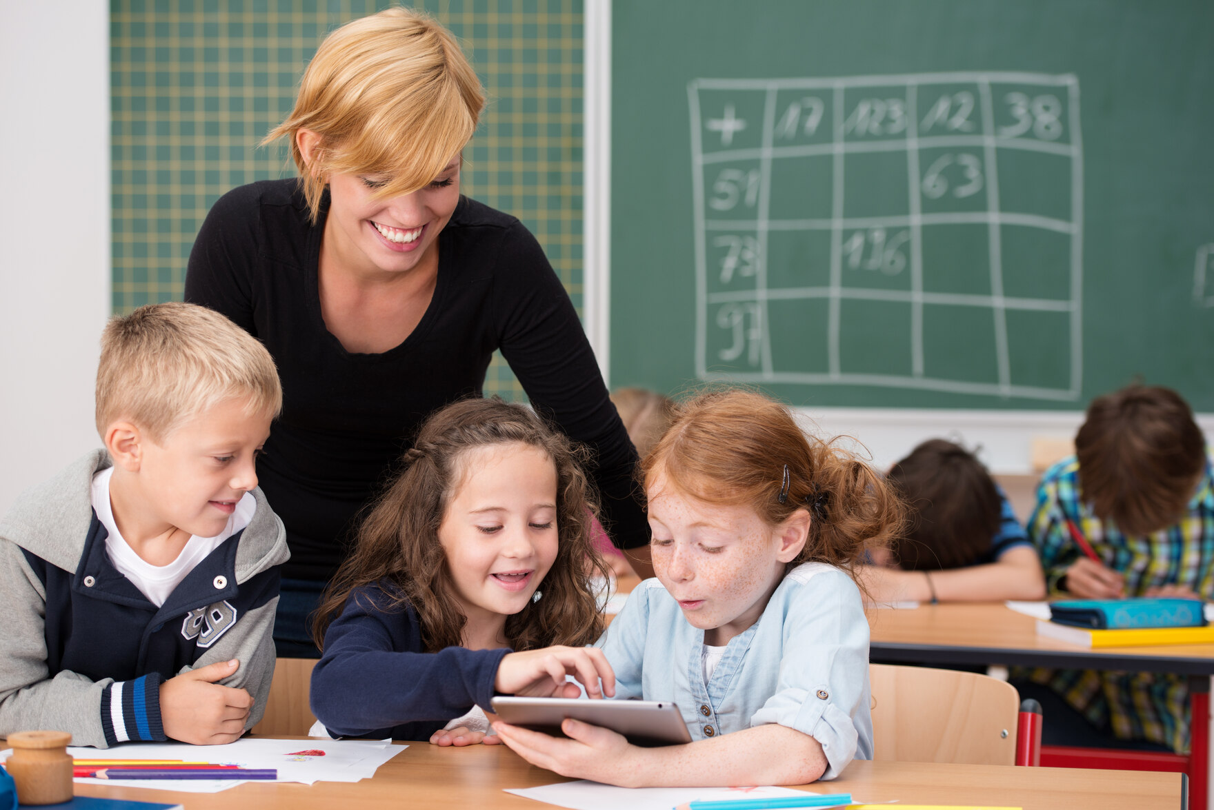 Eine Lehrerin hilft drei Kindern bei der Nutzung eines Tablet-PC im Unterricht