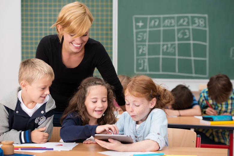 Eine Lehrerin hilft drei Kindern bei der Nutzung eines Tablet-PC im Unterricht