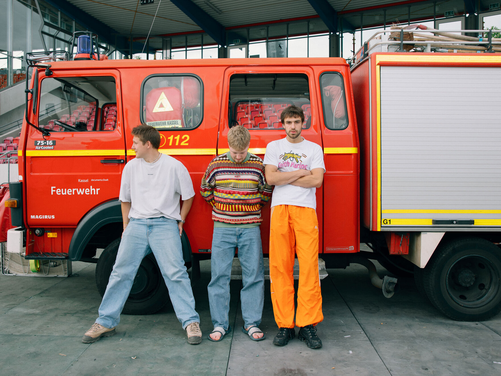 Drei junge Männer stehen vor einer alten Feuerwehr.