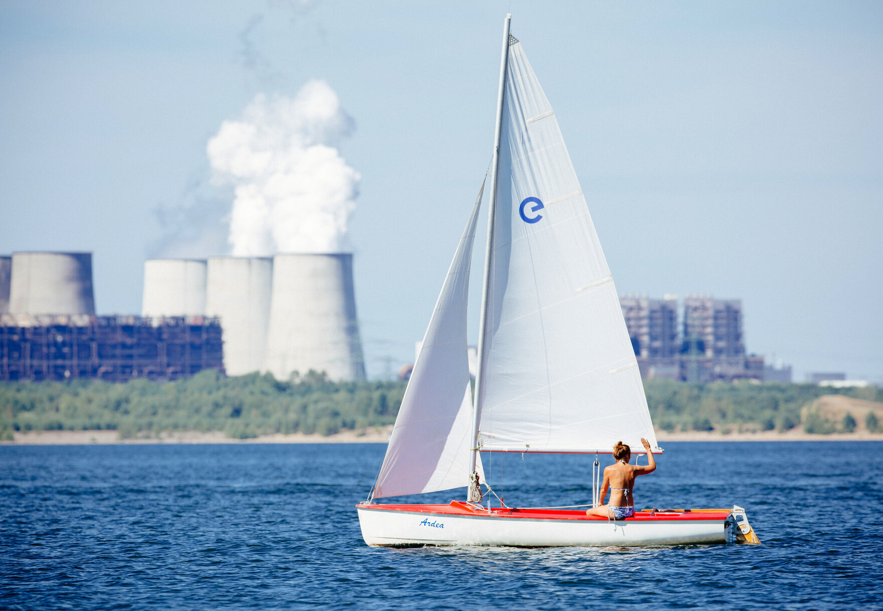 Ein Segelboot auf einem See. Im Hintergrund sind die Kühltürme eines Kraftwerks zu sehen